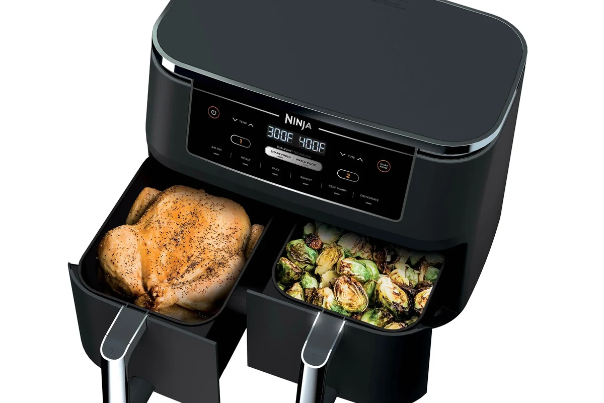 Modern air fryer on a kitchen counter with cooked vegetables and a clean basket