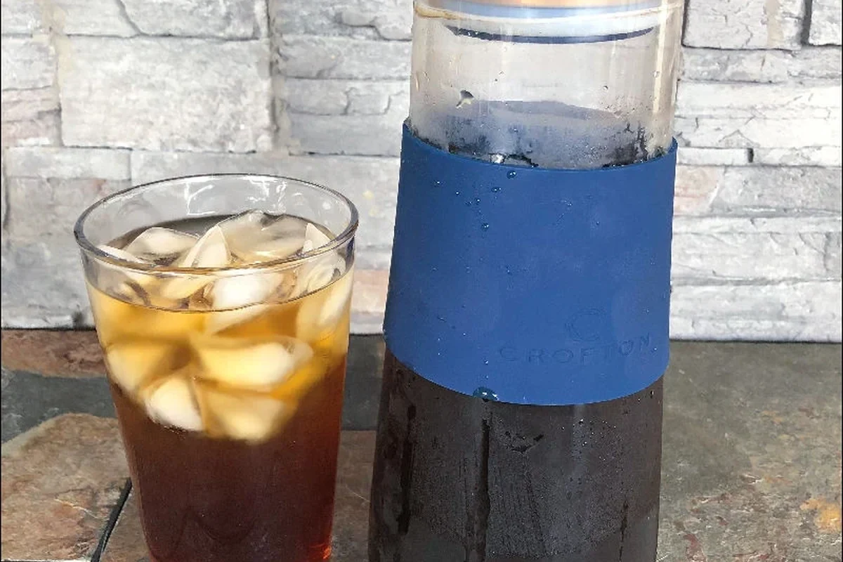 Aldi cold brew coffee maker with coffee grounds, water, and a glass of iced coffee on a kitchen counter