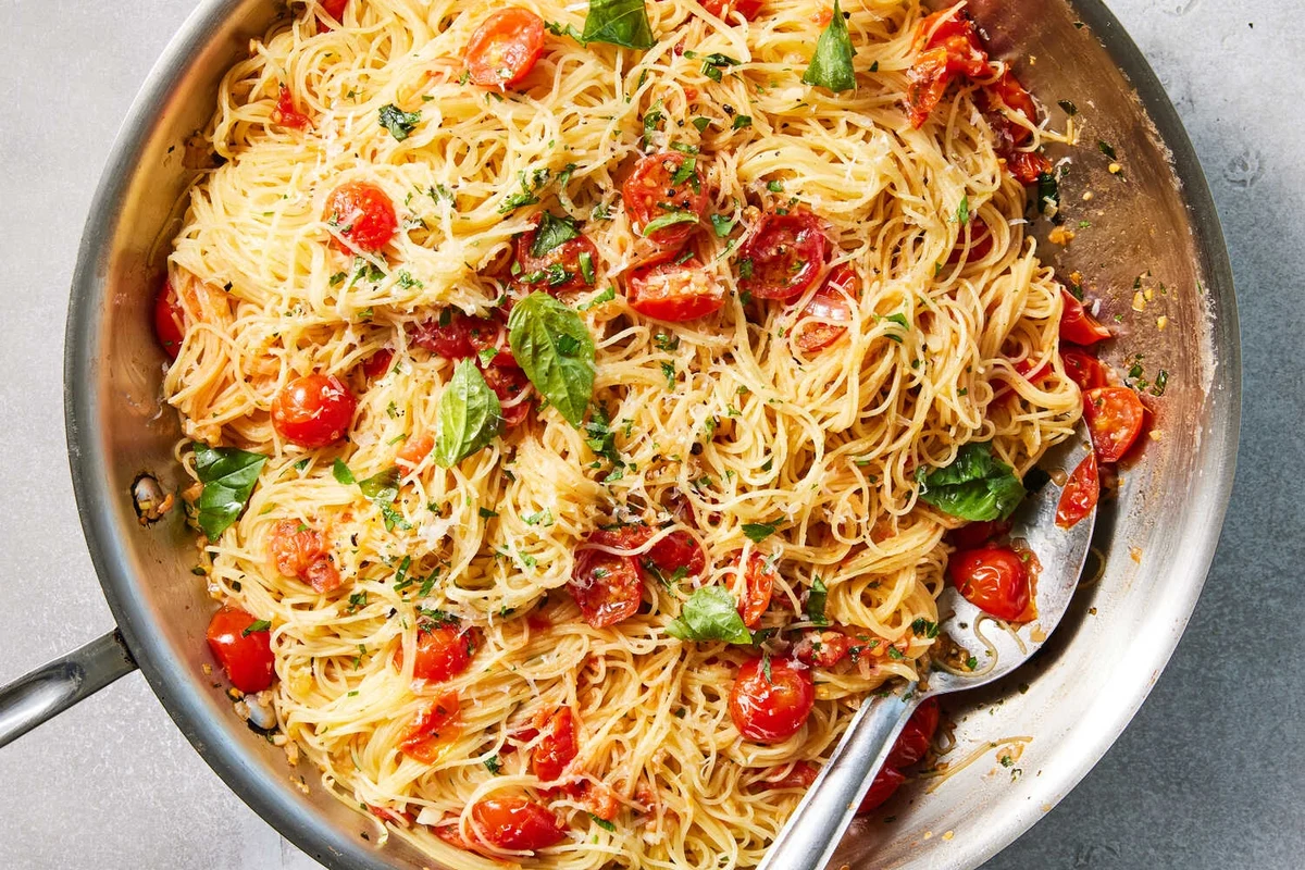 Bowl of angel hair pasta with tomato sauce, vegetables, and herbs on a kitchen table