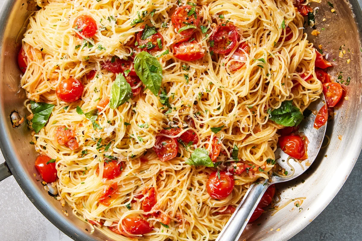 Bowl of angel hair pasta with tomato sauce, vegetables, and herbs on a kitchen table