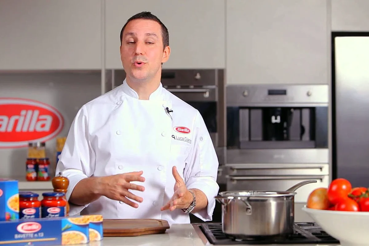 A bowl of Barilla-style pasta with vegetables, tomato sauce, and grilled chicken in a bright kitchen