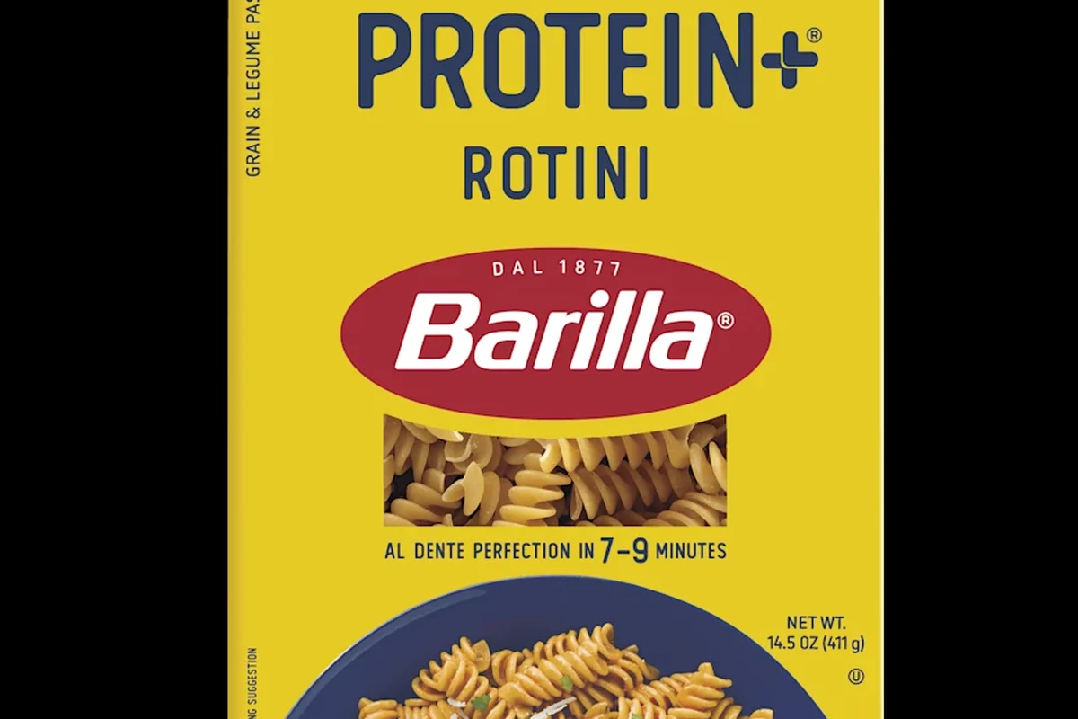 A bowl of Barilla-style pasta with vegetables, tomato sauce, and grilled chicken in a bright kitchen