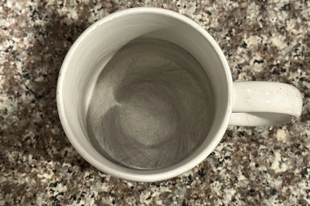 Scratched coffee mug beside mild soap, soft sponge, and baking soda on a kitchen counter