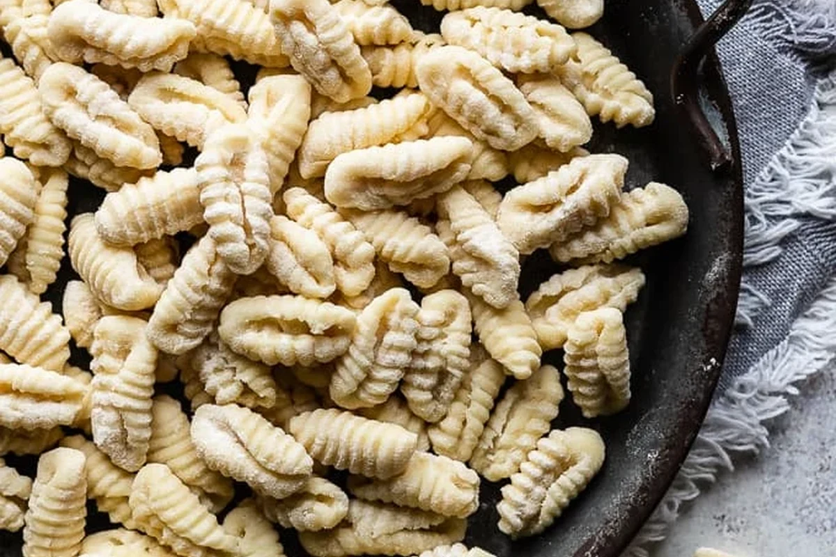 Bowl of cavatelli pasta with tomato sauce and herbs on a kitchen table