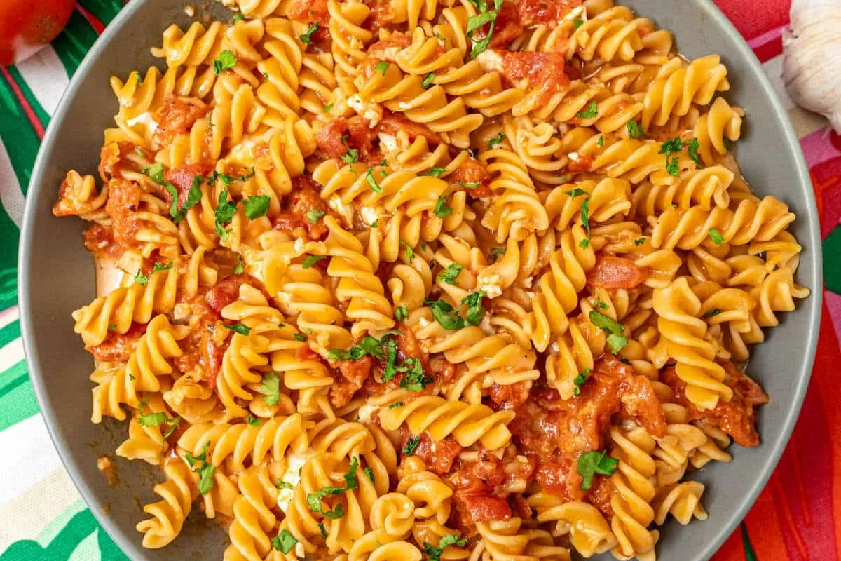 Bowl of cooked chickpea pasta with tomato sauce and herbs in a bright kitchen