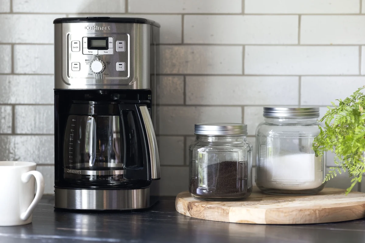 French press coffee in a glass press with coarse grounds and a mug on a kitchen counter
