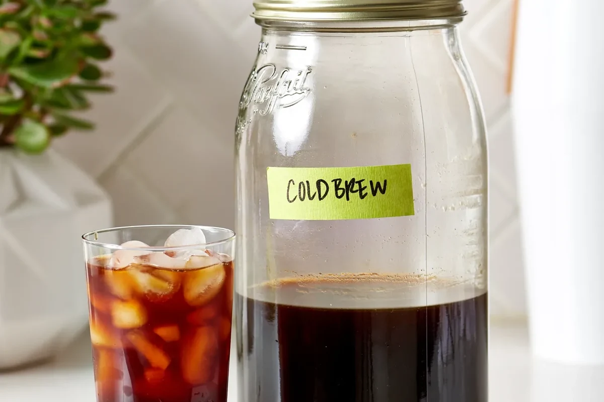 Glass of cold brew coffee beside a clean home brewer and ice on a kitchen counter