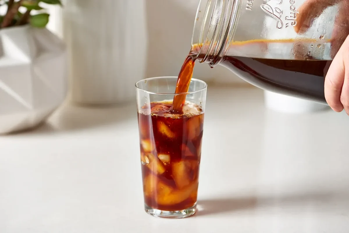 Glass of cold brew coffee beside a clean home brewer and ice on a kitchen counter