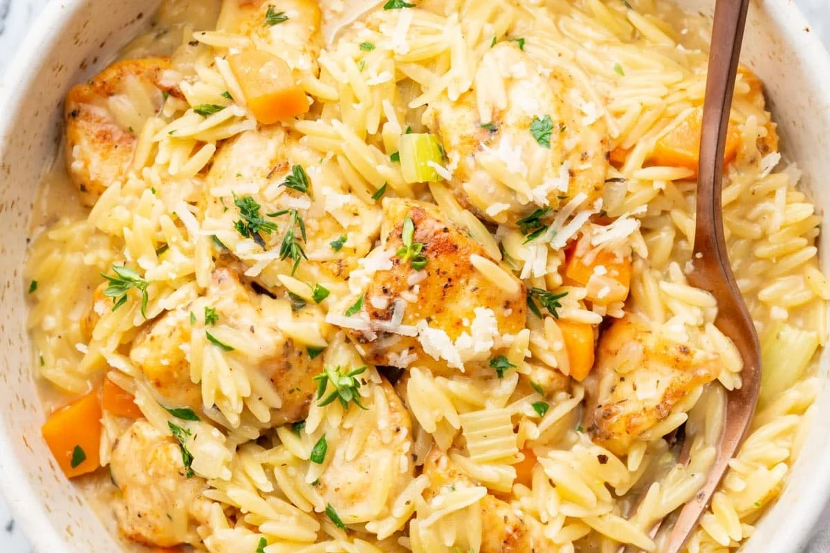 Orzo pasta simmering in chicken broth in a saucepan with a spoon