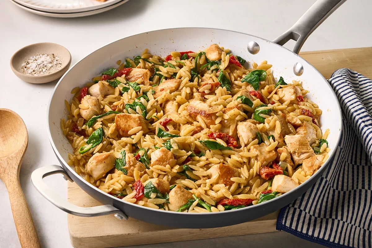 Orzo pasta simmering in chicken broth in a saucepan with a spoon