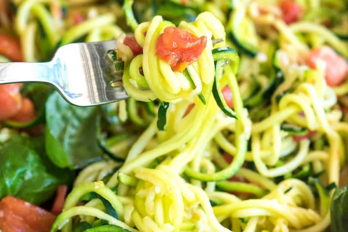 Zucchini noodles tossed with sauce in a skillet on a kitchen counter