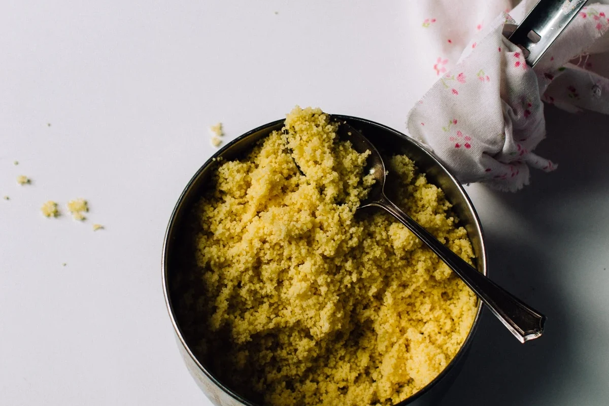 Bowl of fluffy couscous with herbs, lemon, and vegetables on a kitchen counter