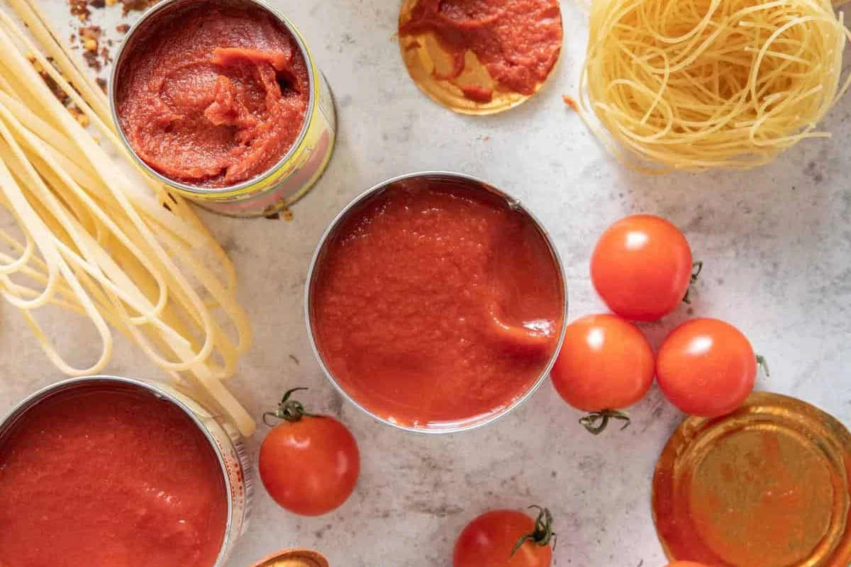 Tomato paste and tomato sauce in bowls on a kitchen counter with pasta ingredients