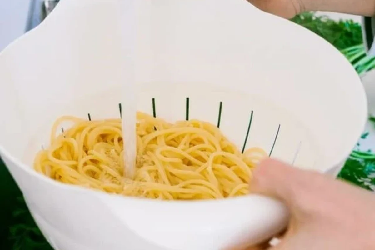 Person draining spaghetti into a colander in a clean home kitchen
