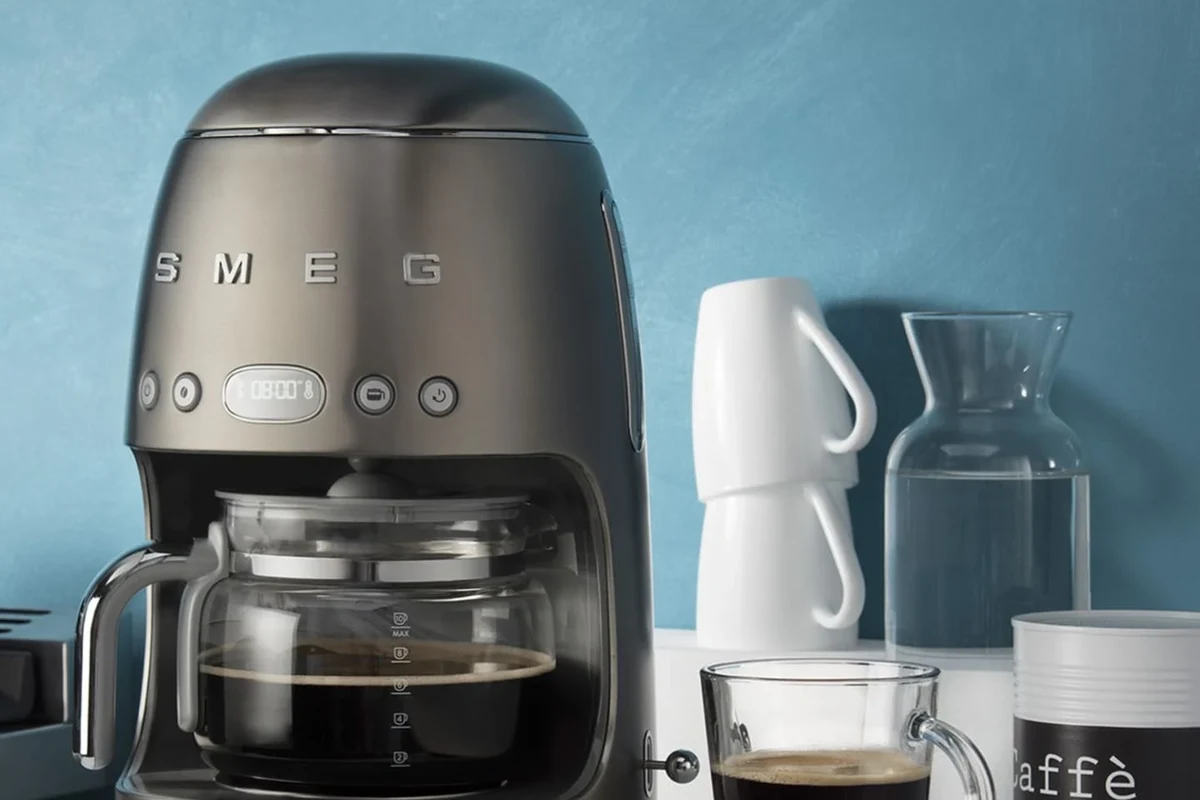 French press coffee brewer with coarse grounds, hot water, and a cup on a kitchen counter