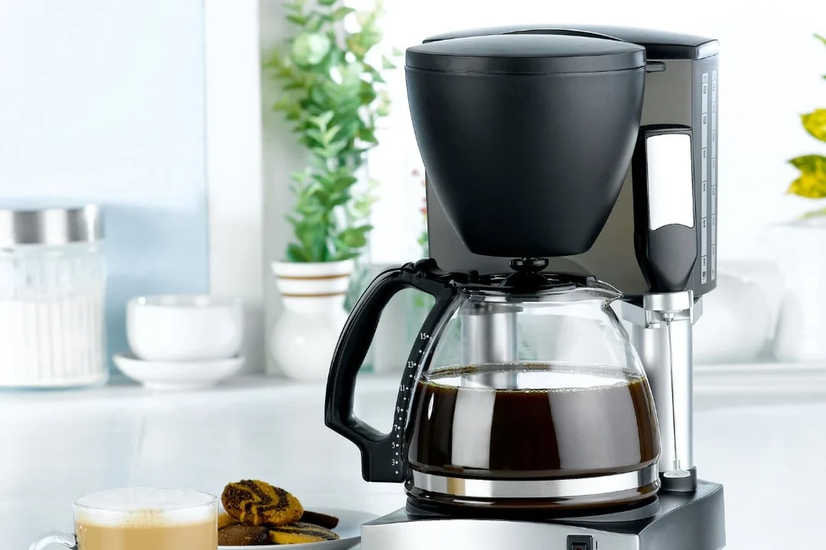 French press coffee maker with grounds, hot water, and plunger on a kitchen counter