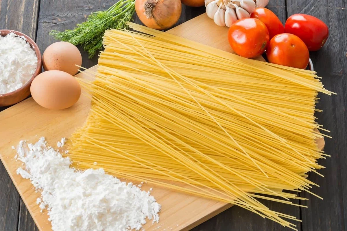 Dry pasta in a pantry container beside a package and measuring cup