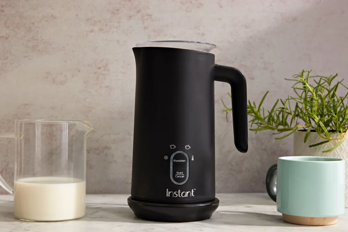 Beginner using an electric milk frother to make foam for coffee in a kitchen