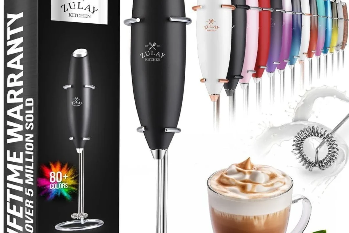 Electric milk frother beside a cup of coffee with milk foam and cleaning tools in a kitchen