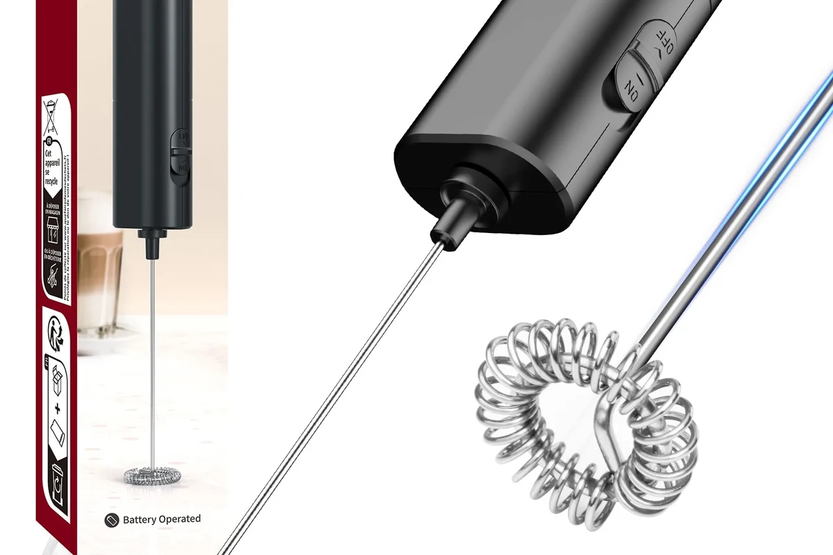 Electric milk frother making foamy milk beside a coffee cup on a kitchen counter