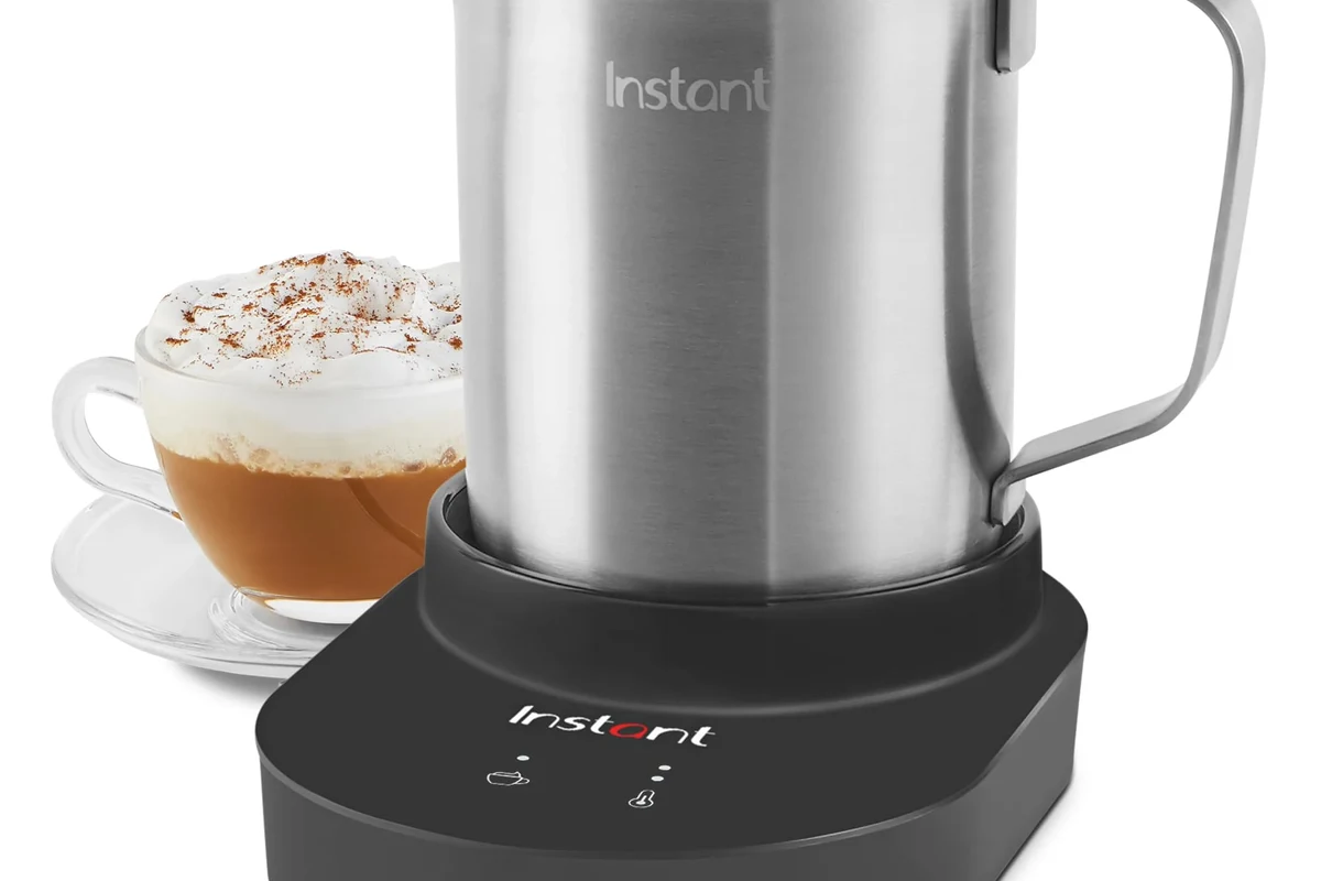 Electric milk frother making creamy foam in a kitchen beside a coffee mug