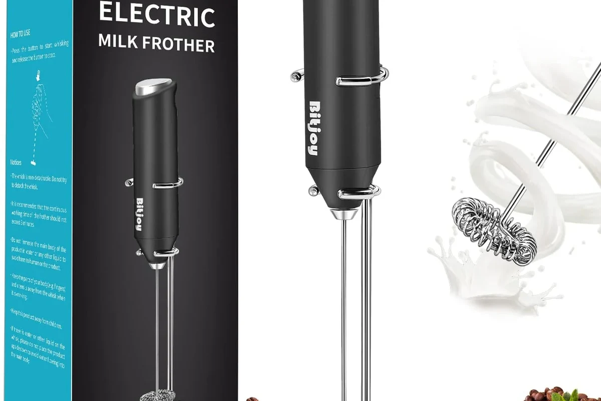 Electric milk frother with fresh foam in a kitchen beside coffee cups