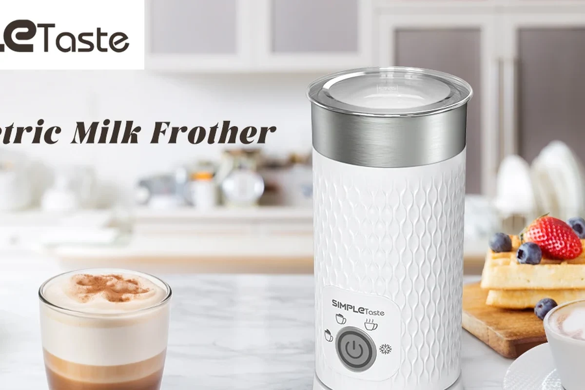 Electric milk frother with fresh foam in a kitchen beside coffee cups
