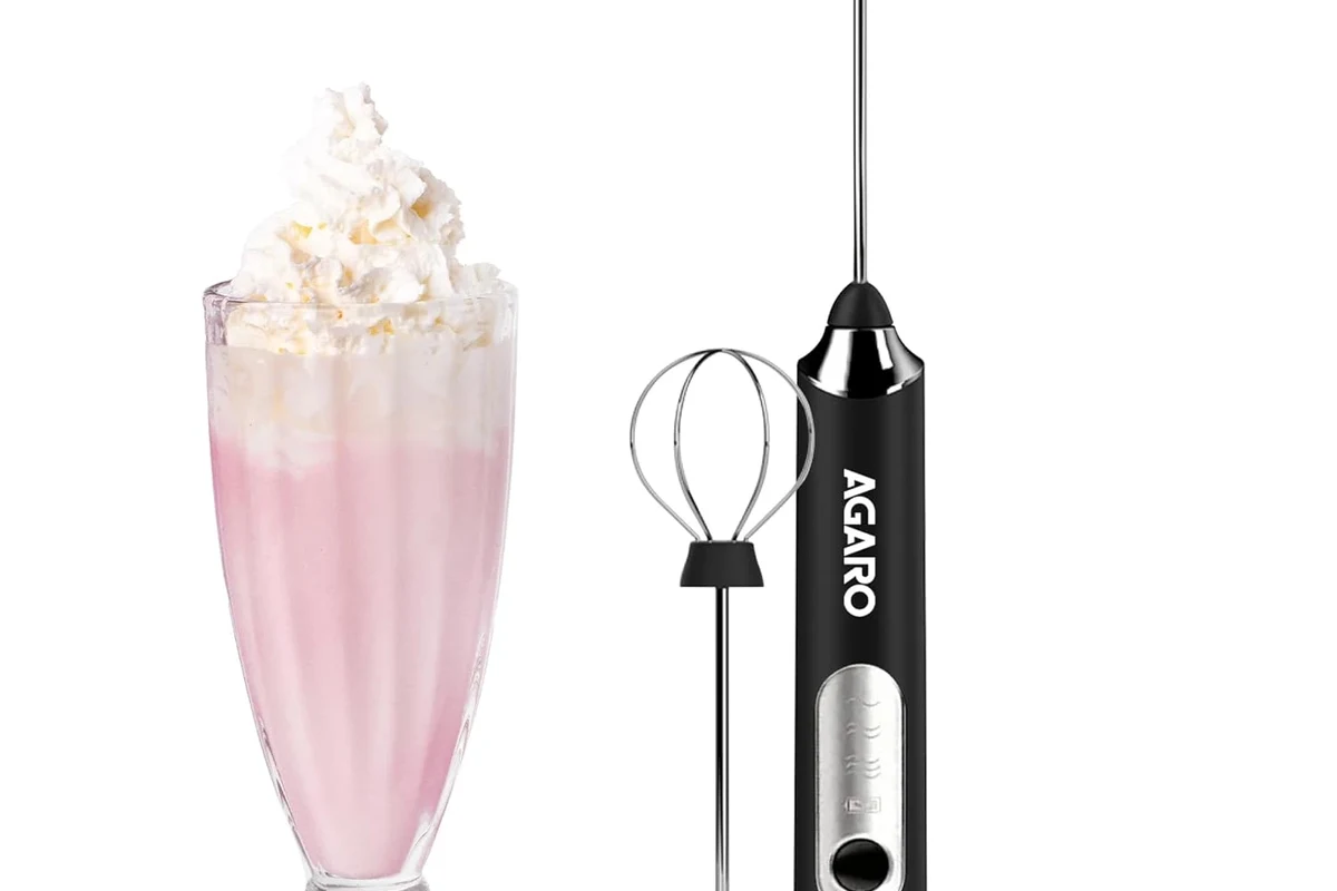 Electric milk frother with warm milk foam beside a home coffee setup