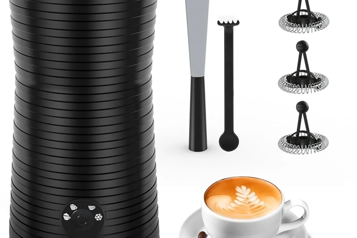 Electric milk frother with warm milk foam beside a home coffee setup