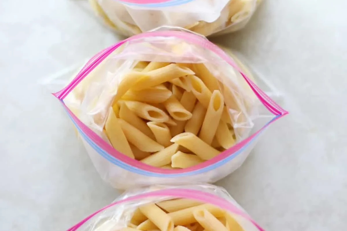 Cooked pasta portions stored in freezer containers beside a bowl of reheated pasta