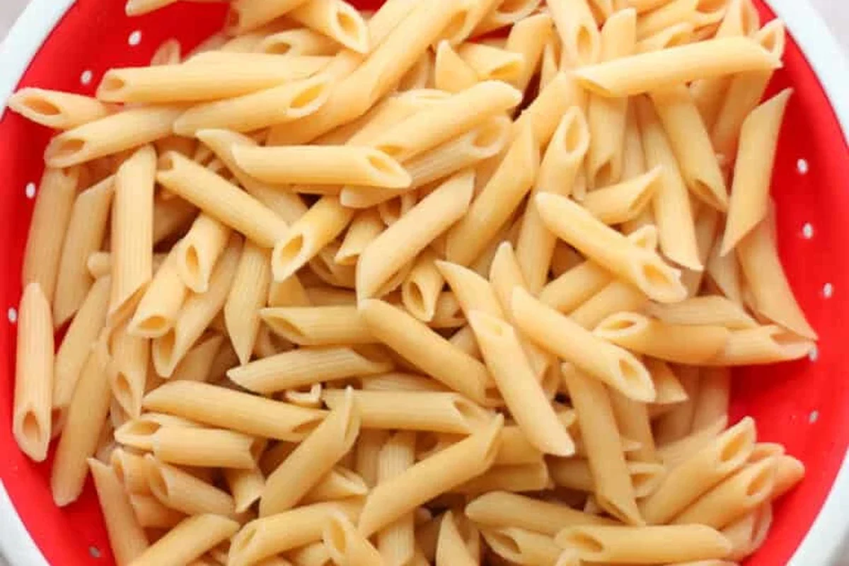 Cooked pasta portions stored in freezer containers beside a bowl of reheated pasta