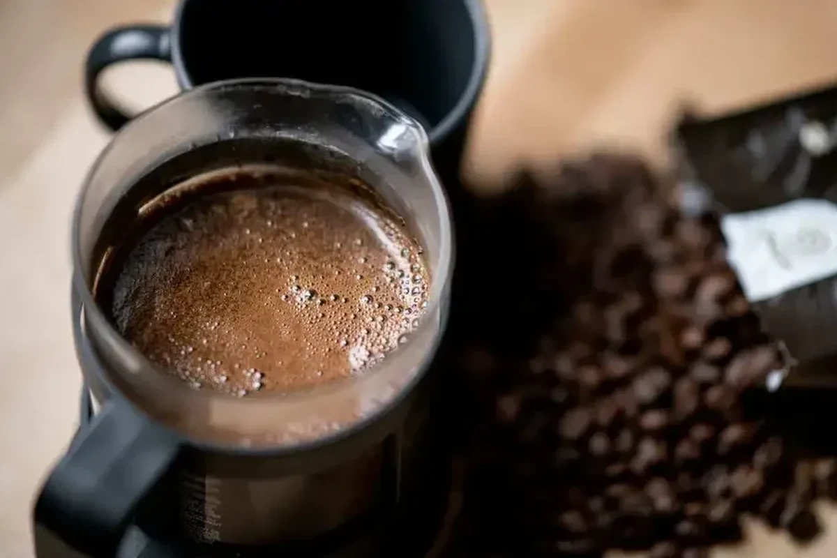 Beginner making French press coffee with coarse grounds, hot water, and a glass press on a kitchen counter