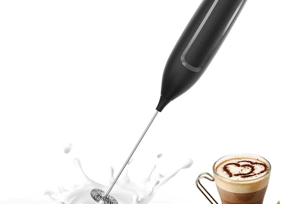 Electric milk frother making thick creamy foam in a kitchen mug beside espresso