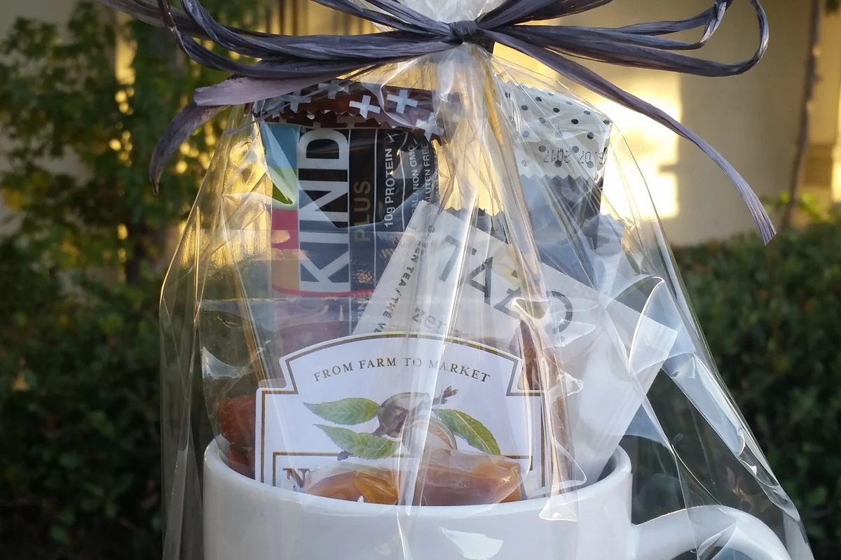 Gift box with a coffee mug, tea, snacks, and a handwritten note on a kitchen counter