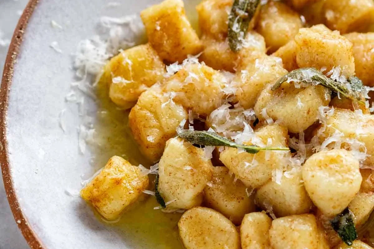 Bowl of potato gnocchi with sauce and herbs in a home kitchen