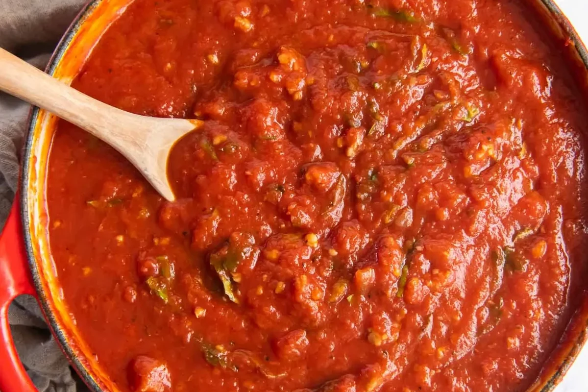 Home canning setup with tomato pasta sauce, jars, lids, funnel, and canner on a kitchen counter