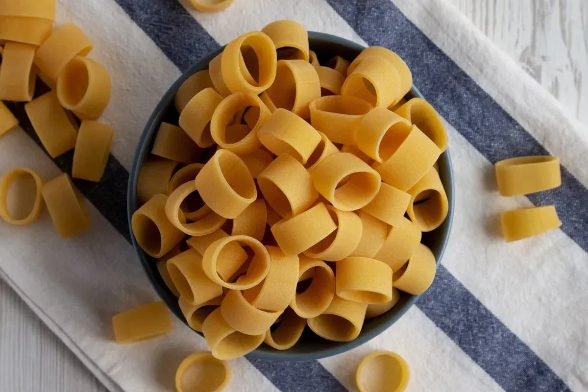 Bowl of dry pasta on a kitchen counter beside a glass of water