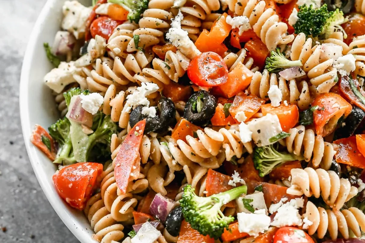 Bowl of Italian pasta salad with vegetables, herbs, cheese, and light dressing on a kitchen table
