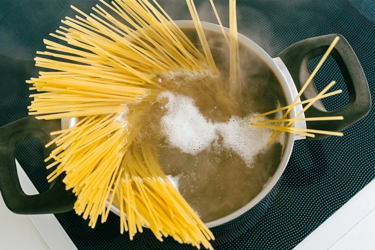 Pot of pasta boiling on a stove with foam rising near the rim in a home kitchen