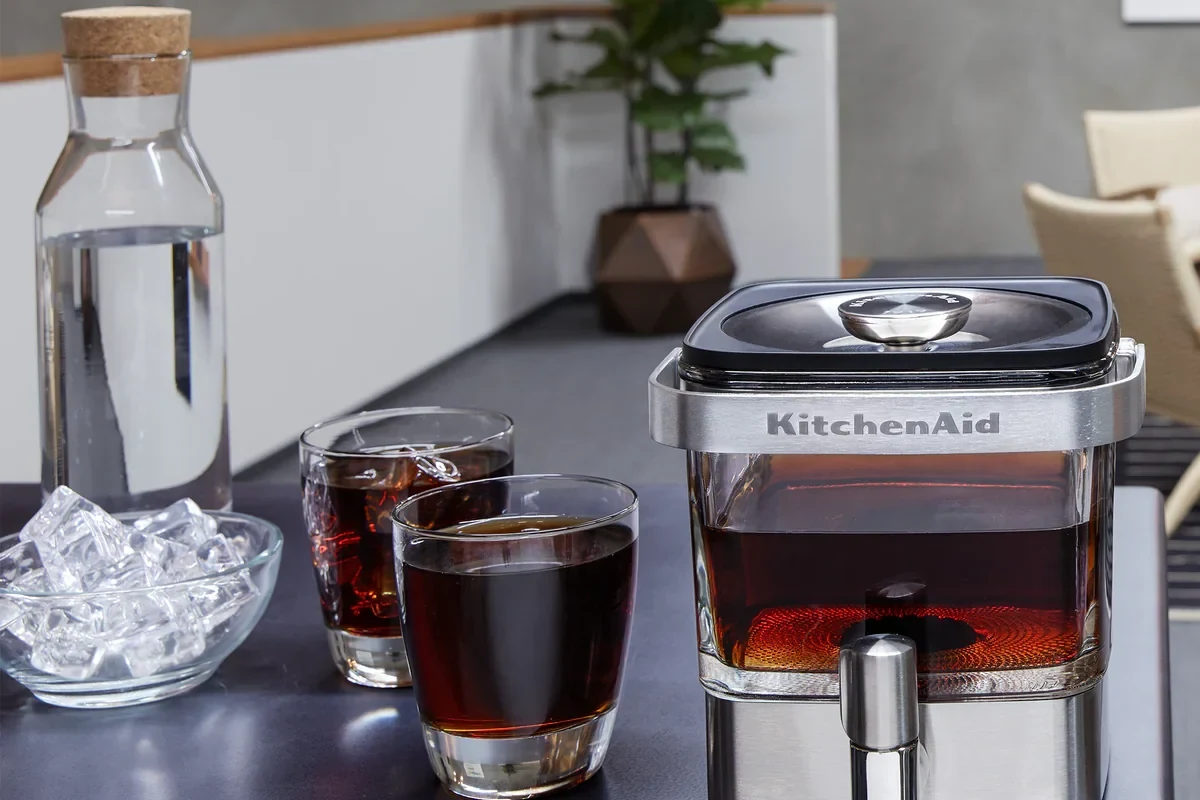 KitchenAid cold brew coffee maker on a counter with coffee grounds and a glass of iced coffee