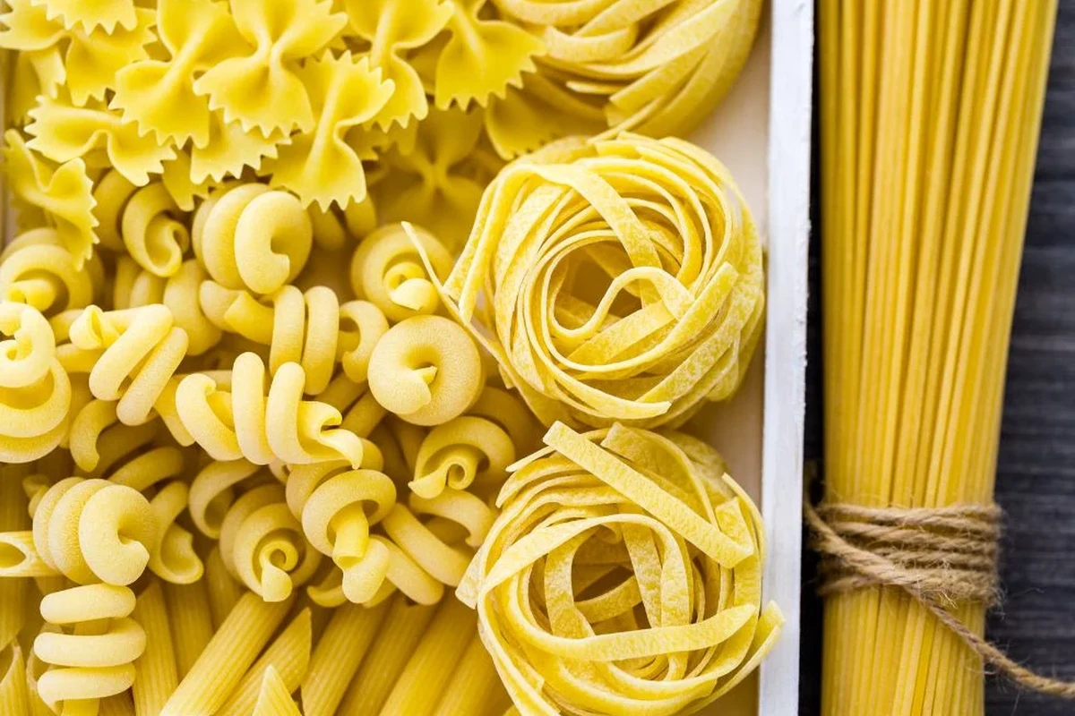 Dry pasta in a pantry container with a date label and a bowl of cooked spaghetti