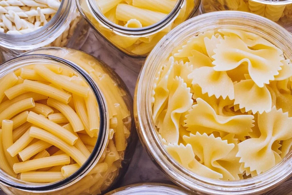Dry pasta in a pantry container with a date label and a bowl of cooked spaghetti