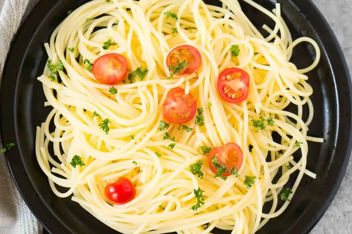 Pot of boiling pasta with tongs and a timer on a home kitchen stove