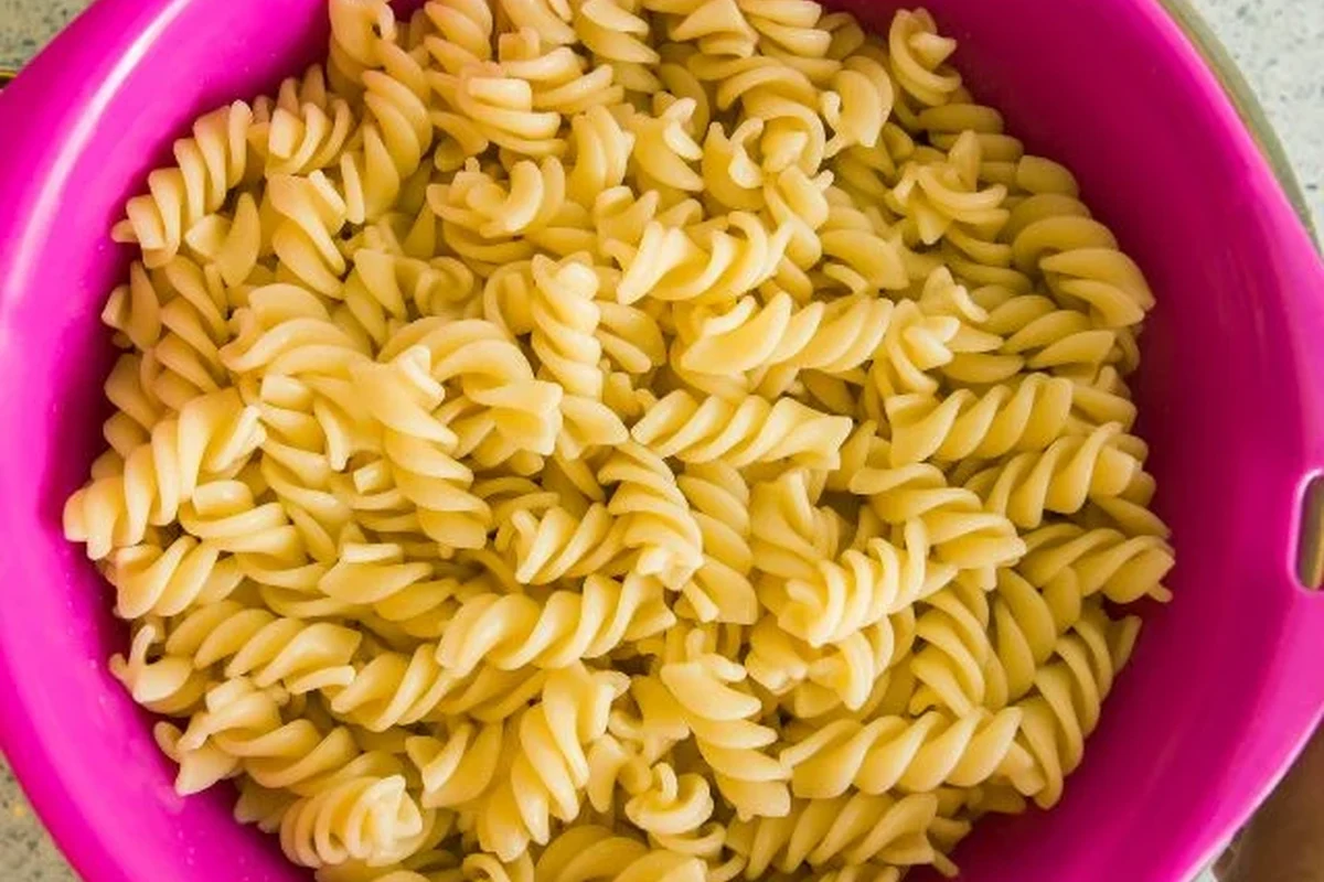 Cooked pasta in a bowl on a kitchen counter with a timer and storage containers nearby