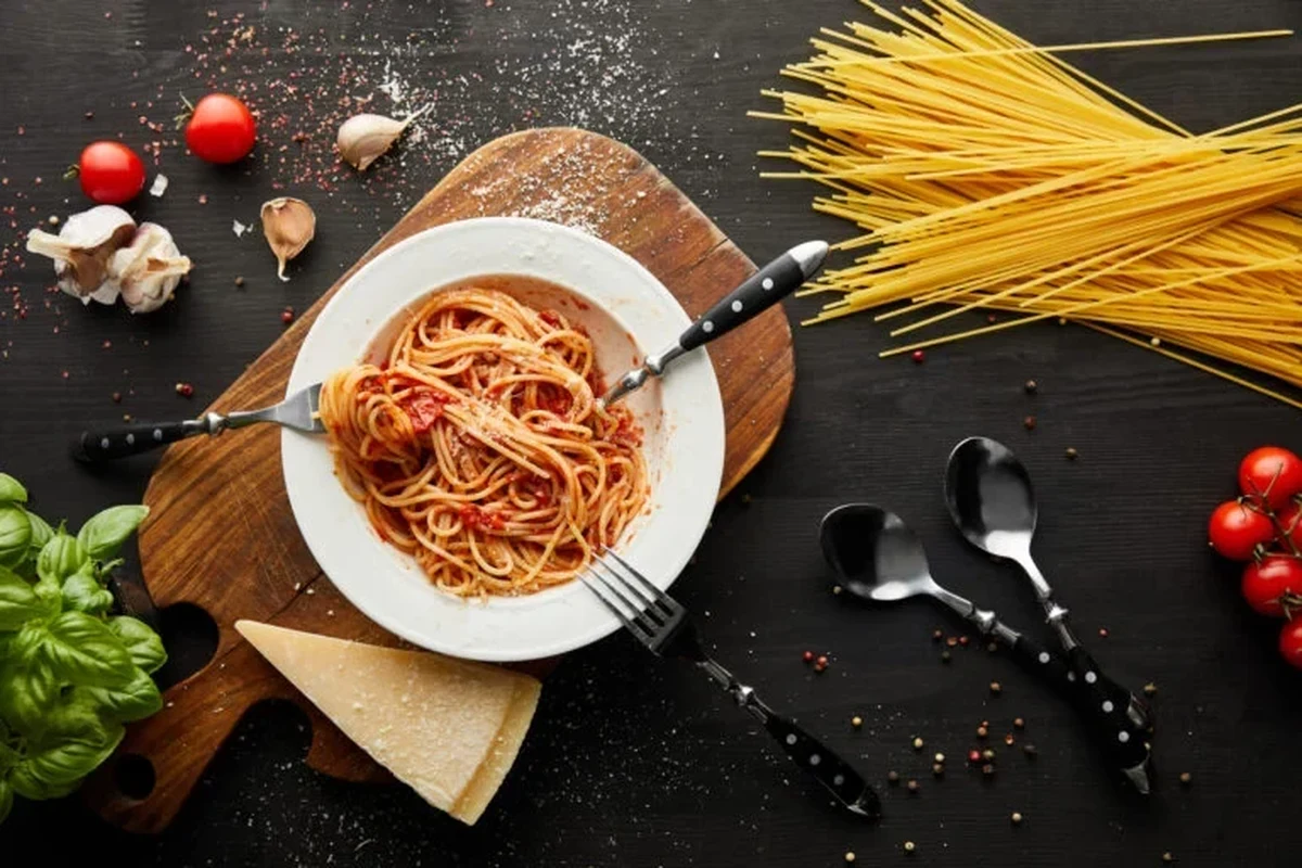 Cooked pasta in a bowl on a kitchen counter with a timer and storage containers nearby