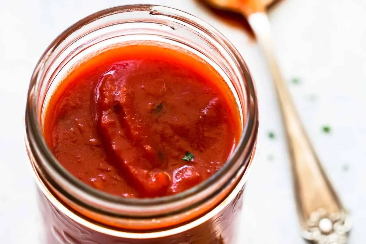 Small saucepan of tomato sauce made from tomato paste with spoon and ingredients nearby