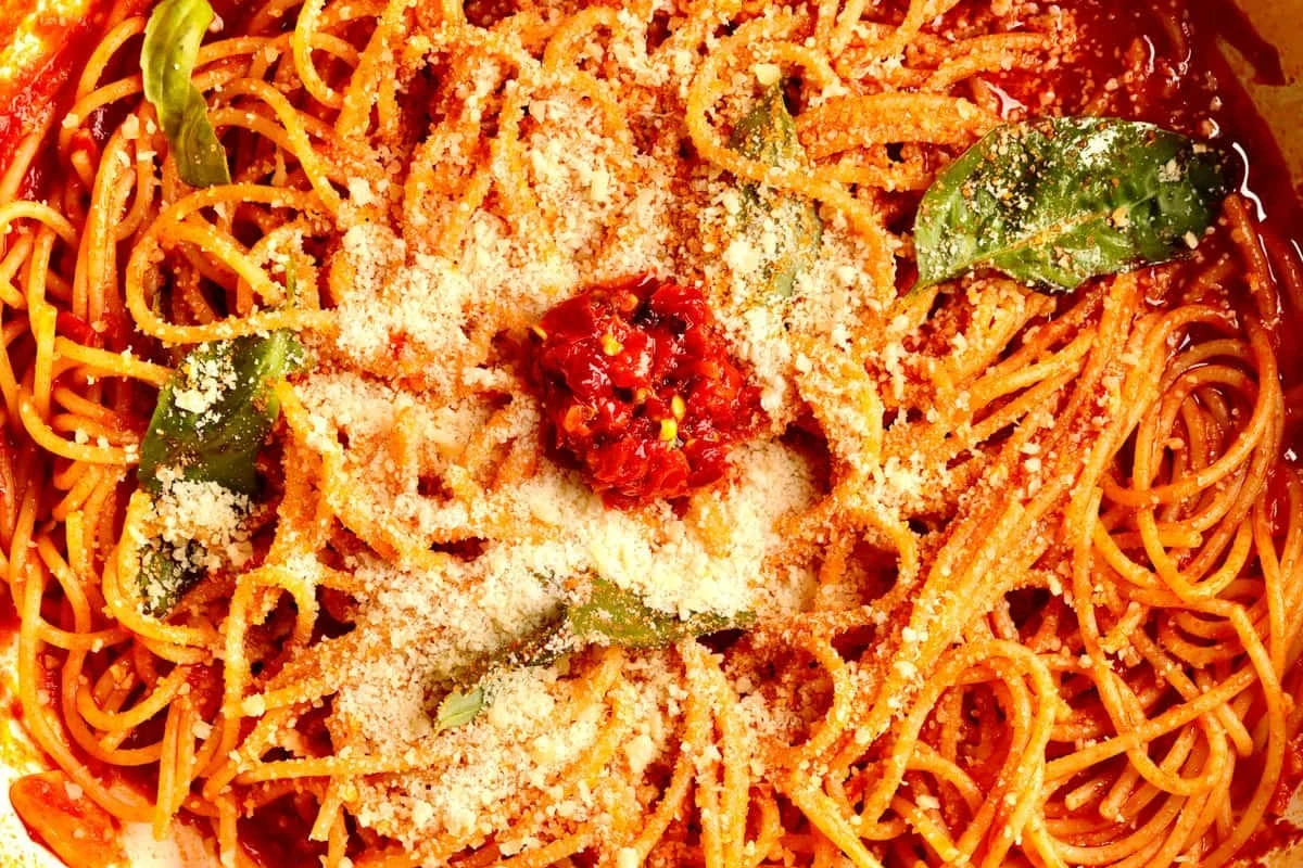 Small saucepan of tomato sauce made from tomato paste with spoon and ingredients nearby