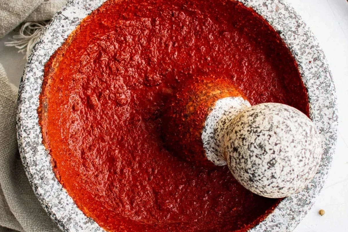 Homemade achiote paste in a bowl with annatto seeds, garlic, and spices on a kitchen counter