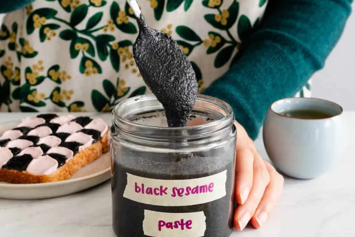 Black sesame paste in a bowl with toasted sesame seeds and a spoon in a home kitchen