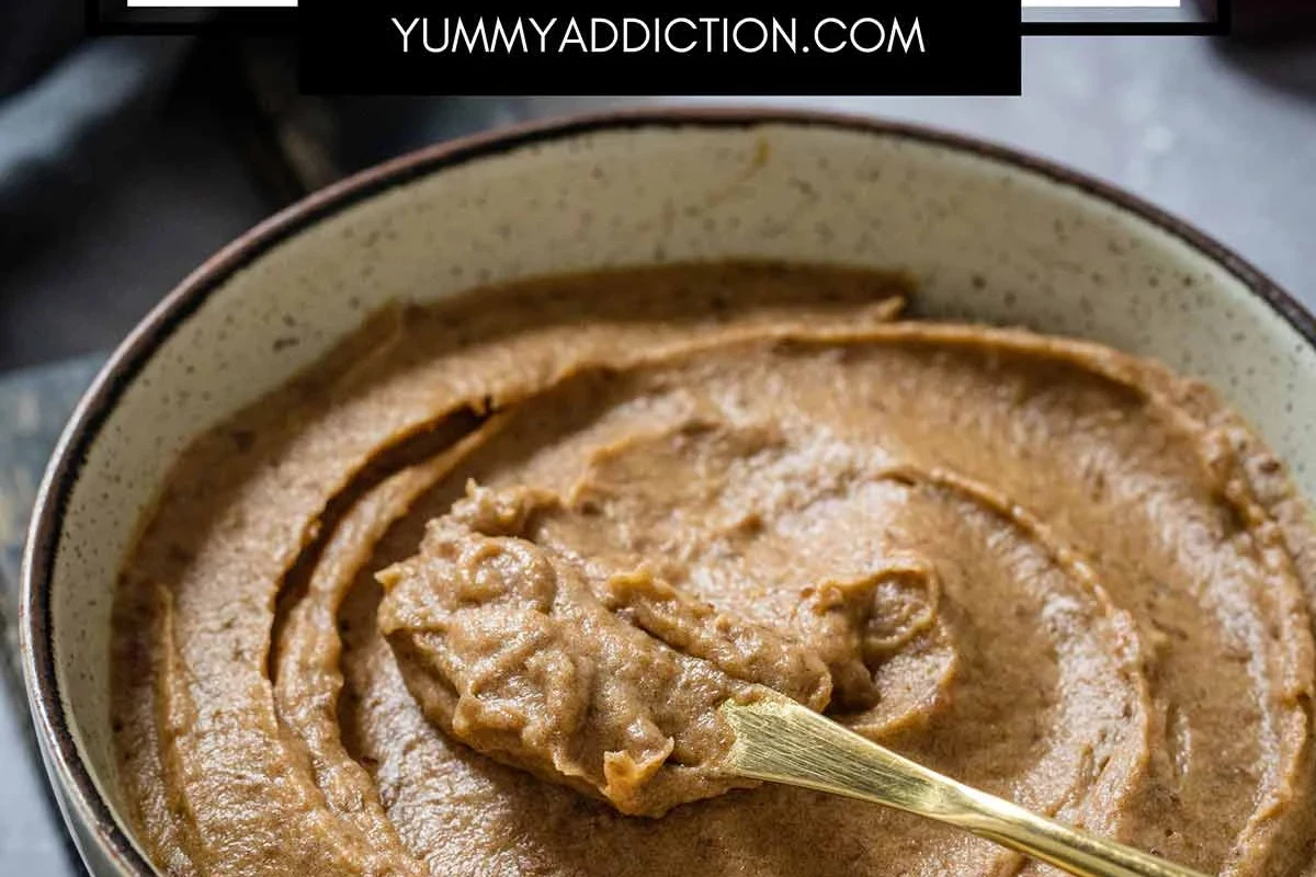 Homemade date paste in a bowl with dates, a blender, and a spoon on a kitchen counter